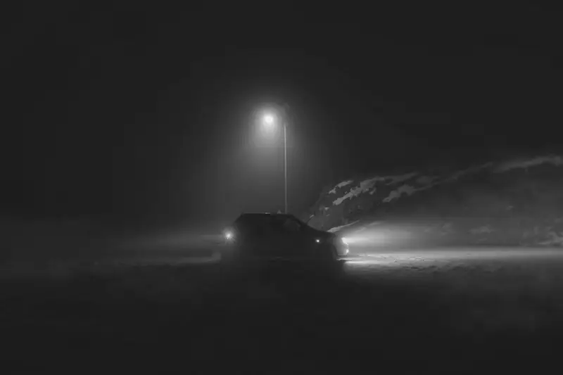 Auto bei Nacht im Nebel, Scheinwerfer und Rücklicht an, dahinter eine Straßenlaterne
