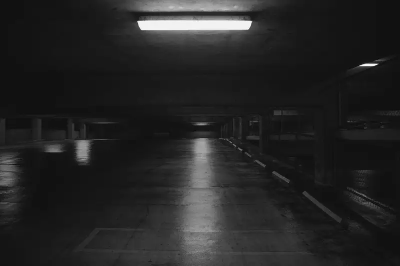Leere Tiefgarage bei Nacht, eine einzelne Leuchtstoffröhre an der Decke, auf dem Boden eine markierte Parkfläche